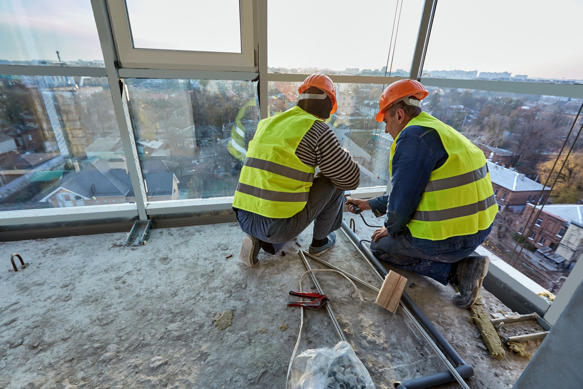 Two workers in protective clothing and safety helmets installing plastic pipes using soldering iron on balcony of flat of building under construction